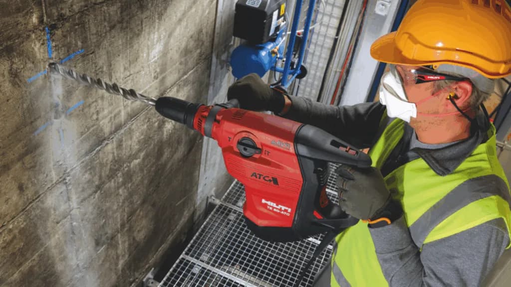 An operator using a hammer drill with dust control fitted.