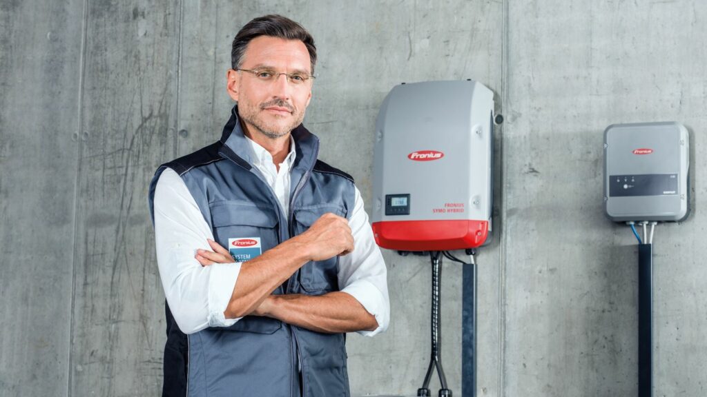 Fronius Solutions Partner FSP standing in-front of a Fronius Hybrid Inverter with arms folded